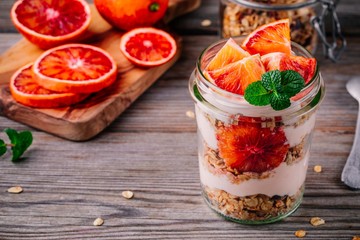 healthy breakfast  glass jar yoghurt parfait with homemade granola and blood orange on a wooden...