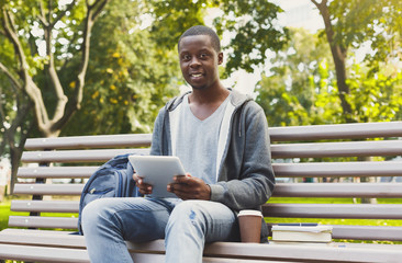 Obraz premium Smiling african-american student in the park with tablet oudoors