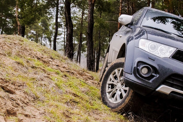 large black SUV stands inclined on a sandy hill in the forest