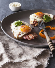 Sandwich, toast with bacon, sauce and poached egg on grey plate on dark background vertically.