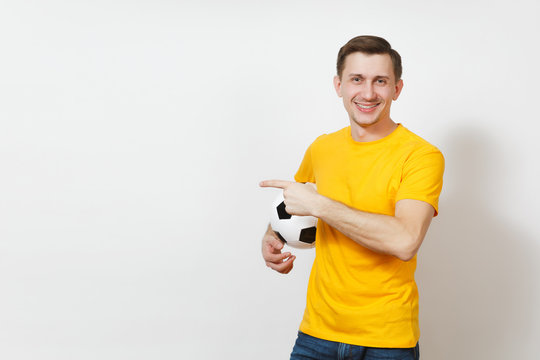 Inspired young European man, fan or player in yellow uniform hold soccer ball point index finger aside cheer favorite football team isolated on white background. Sport play football lifestyle concept.