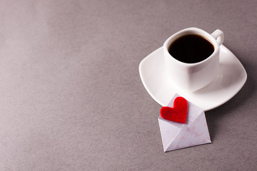 a cup of espresso and a love message in a small envelope on a gray background, laconism, minimalism