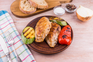 Fried chicken fillet with grilled vegetables in a plate on a rustic wooden table