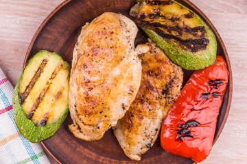 Fried chicken fillet with grilled vegetables in a plate on a rustic wooden table - close-up