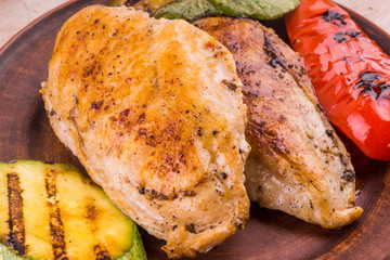 Fried chicken fillet with grilled vegetables in a plate on a rustic wooden table - close-up