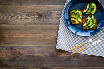 Idea for a healthy and nutritious breakfast. Plate with avocado toast with wholegrain bread on dark wooden background top view copy space