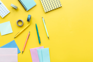 Scattered stationery on student's desk. Yellow background top view copy space