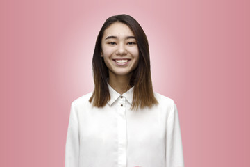 Fototapeta premium Indoor portrait of young attractive and very happy woman smiling in white formal shirt on the rose background. Emotions, feelings, lifestyle concept