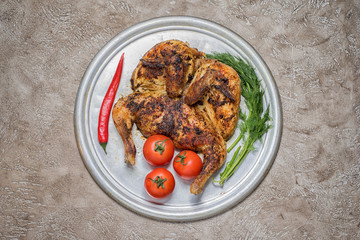 roasted tobacco chicken on a metal round tray in the center of a beige cement background, top view with copy space on the sides.