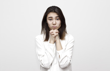 Indoor shot of regretful woman looks gloomy and desperate, keeps hands together, beggs for...