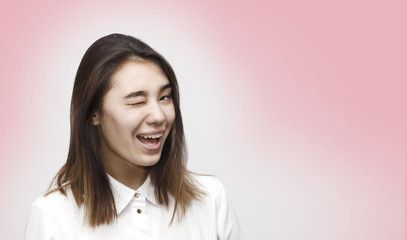 Fototapeta premium Indoor close up portrait of young attractive charming woman winking dressed in formal white shirt. Facial expressions, emotions, lifestyle concept