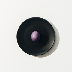 top view of purple easter egg on black plate, on white