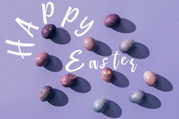 painted chicken eggs on purple background with Happy Easter lettering