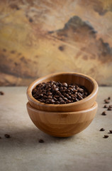 Roasted coffee beans in a wooden bowl on concrete background, selective focus, copy space.