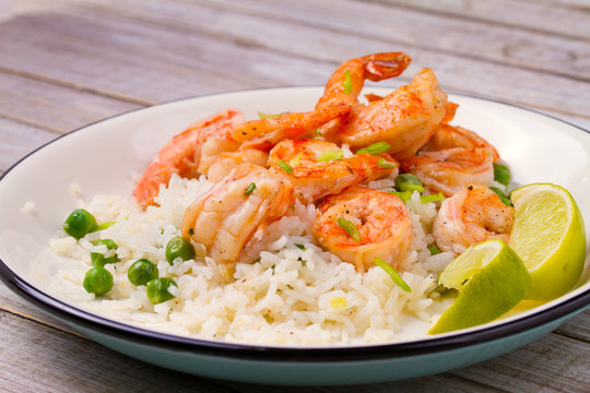 Shrimps with ginger rice and green peas, lime on white plate on wooden background