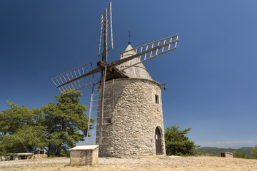 Fototapeta na wymiar Old stone windmill and small group of green trees from one side with clear blue sky in Provence, France 
