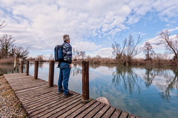 Hiker with backpack over wood pier on shore of river.