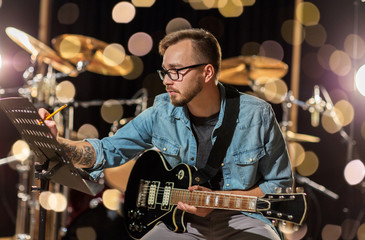 man with guitar writing to music book at studio