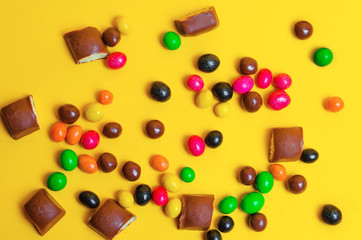 chocolate bars, colorful candies, sweets on a yellow background, top view