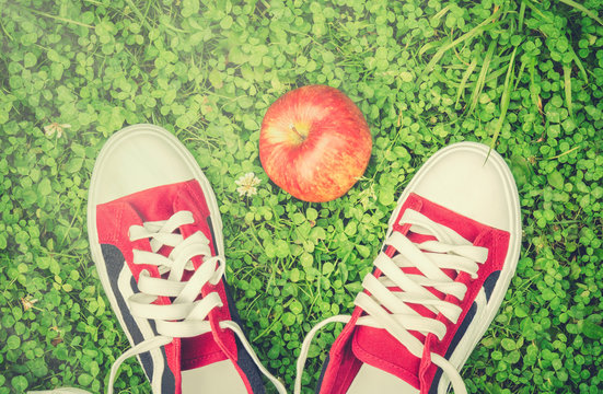 Sports shoes and red apple on green grass. Top view.