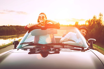 Traveling by car - couple in love go by cabriolet car in sunset time
