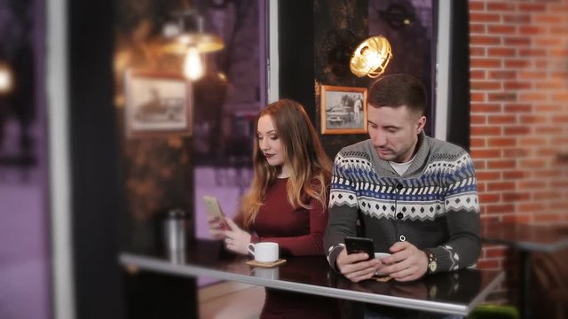 Young couple using and staring at smartphone while sitting in cafe