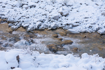 Fluss durch den verschneiten weissen Wald mit Steinen
