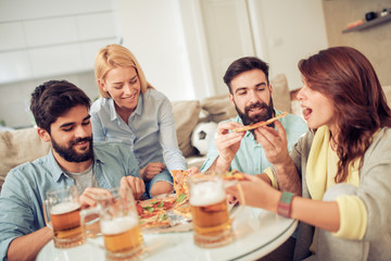 Smiling friends eating pizza and drinking beer at home