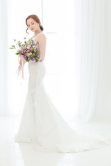 Bride in a wedding dress against a light window.