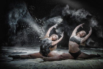 Two girls dance with flour on black background