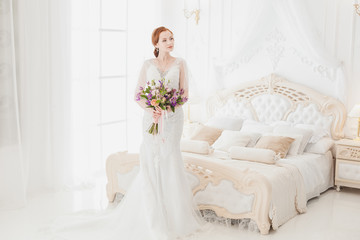 Fototapeta na wymiar Gentle bride in a wedding dress is in the bedroom. Preparation of the bride for the wedding.