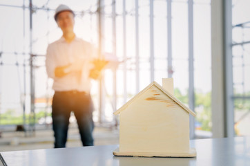 wooden house model with blurred view of technician, architect or engineer in background at construction site, planning start up new project, successful, industry, architecture, housing project concept