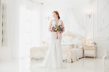 Fototapeta na wymiar Bride in the wedding dress is standing in the royal bedroom, she is waiting for her fiance.