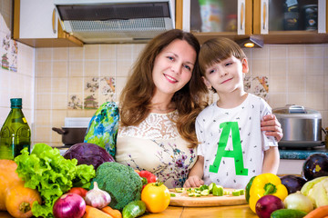 The young cook mother standing with her little son in the kitchen and salting vegetables