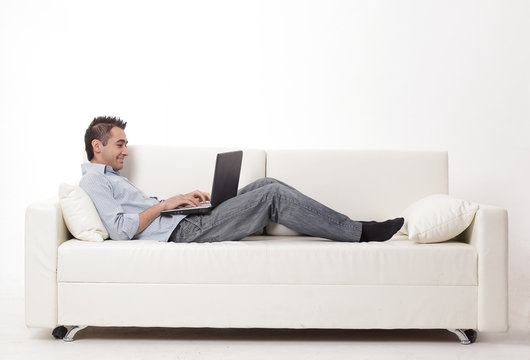 man working on laptop lying on a sofa