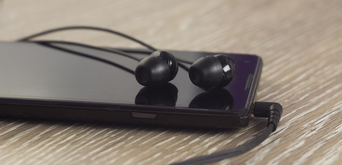 Phone with black headphones on a wooden background