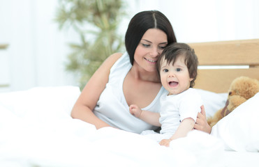 Fototapeta na wymiar Beautiful young mother with a baby lying in bed and smiling