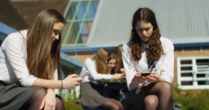 4K School girls looking at smartphones outside school building. Checking social media but not communicating with each other. Slow motion