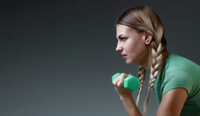 young slender girl works with small dumbbells performing exercises. concept of a healthy lifestyle. Gray background. studio light