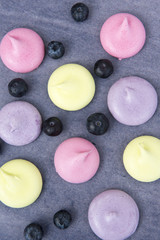Vertical image of pink, green and purple meringues on a grey background with blueberries