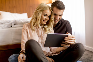 Loving couple sitting on the floor in bedroom and using  tablet