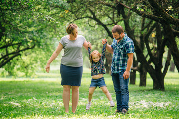 Fototapeta premium Cute young happy family having fun in the park. Little girl with parents outdoors. Mother father and daughter.