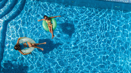 Aerial top view of children in swimming pool from above, happy kids swim on inflatable ring donuts and have fun in water on family holiday vacation on resort

