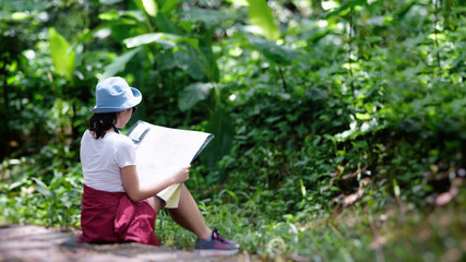 Naklejka na ściany i meble Young Asian female hikers in forest with backpack holding a map in the countryside .Camp Forest Adventure Travel Remote Relax Concept .