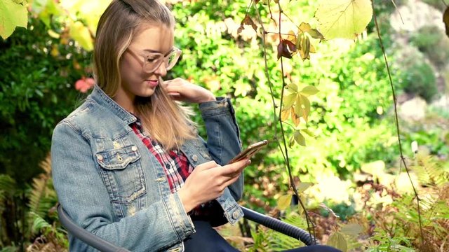 Young woman sitting with smartphone in beautiful garden
