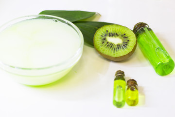Kiwi oil skin and hair care home spa. Bottle of oil, cup with cream, green leaf. White board background