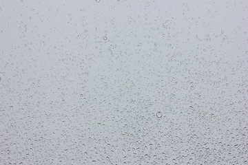 Rain drops on glass against the grey rainy sky