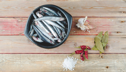 Fresh anchovies in black bowl on wooden background. Top view.