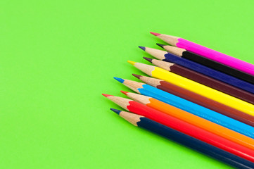 Row of colorful wooden pencils on background of green paper