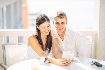 Attractive couple having first date.Coffee with a friend.Smiling happy people making a selfie.Sharing on social media.Showing content on smartphone.Looking something on a device.Modern communication